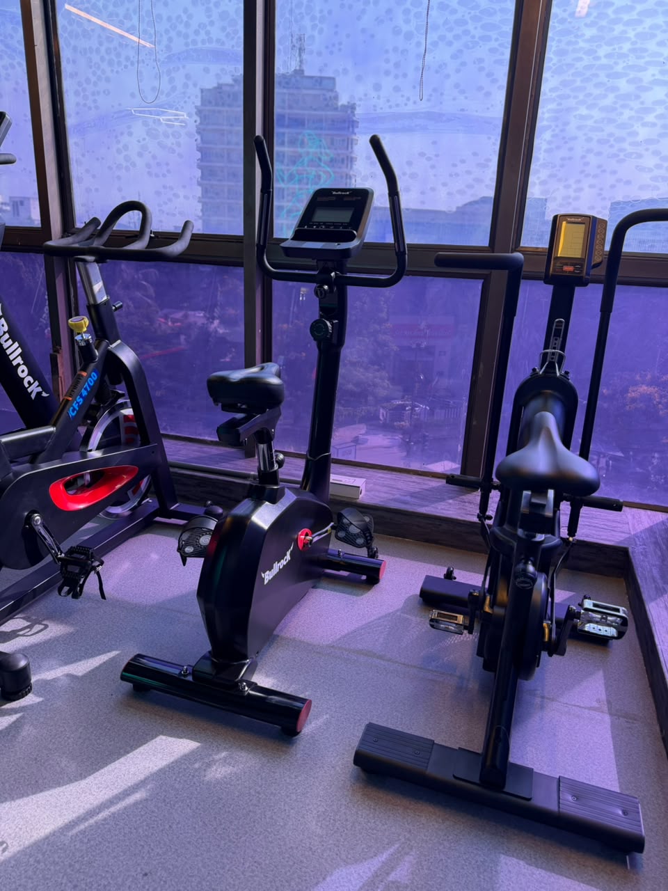 Spin bikes and upright bikes near floor-to-ceiling windows